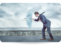 A young business man holding an umbrella to shield himself against a strong headwind. Conceptual image depicting adversity
